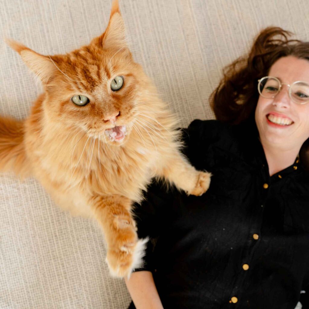 rote Katze steht mit Vorderbeinen auf Frau, die auf dem Boden liegt